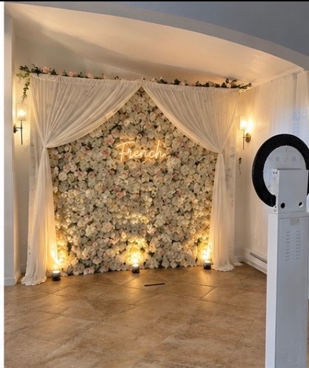 Standard photo booth setup with cream and blush floral flower wall, French neon sign, and warm uplighting
